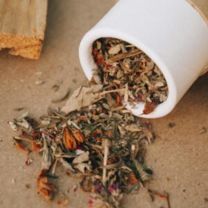 A close-up of dried herbs spilling from a cardboard tube in a natural setting.
