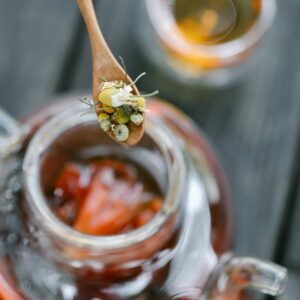 Close-up of chamomile flowers on a wooden spoon over a teapot with brewed tea.