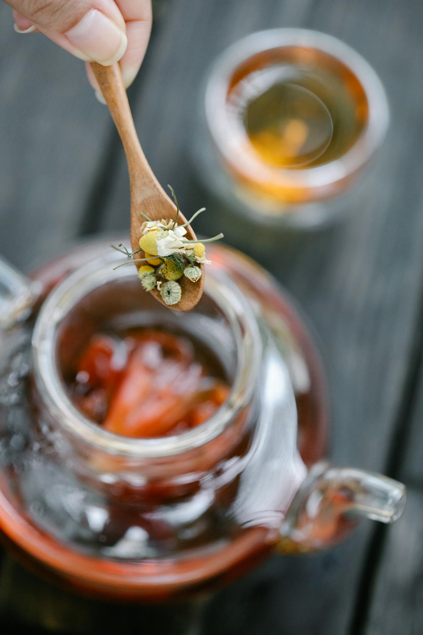 Close-up of chamomile flowers on a wooden spoon over a teapot with brewed tea.