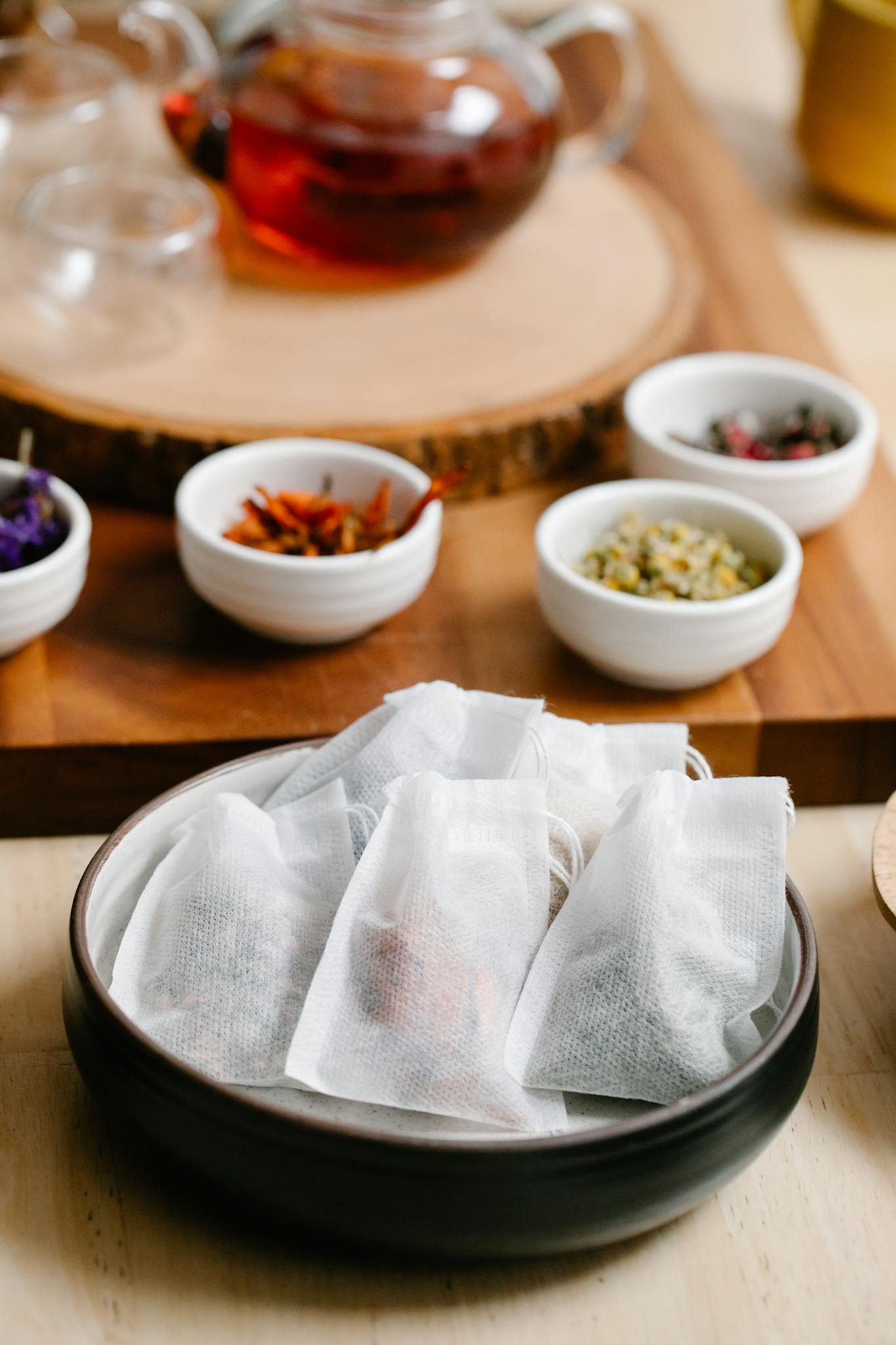 Close-up of herbal tea bags and bowls of dried herbs on a wooden table for brewing.